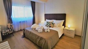 Une chambre d’hôtel avec un grand lit, une table de chevet avec une lampe, une chaise et une fenêtre avec des rideaux.