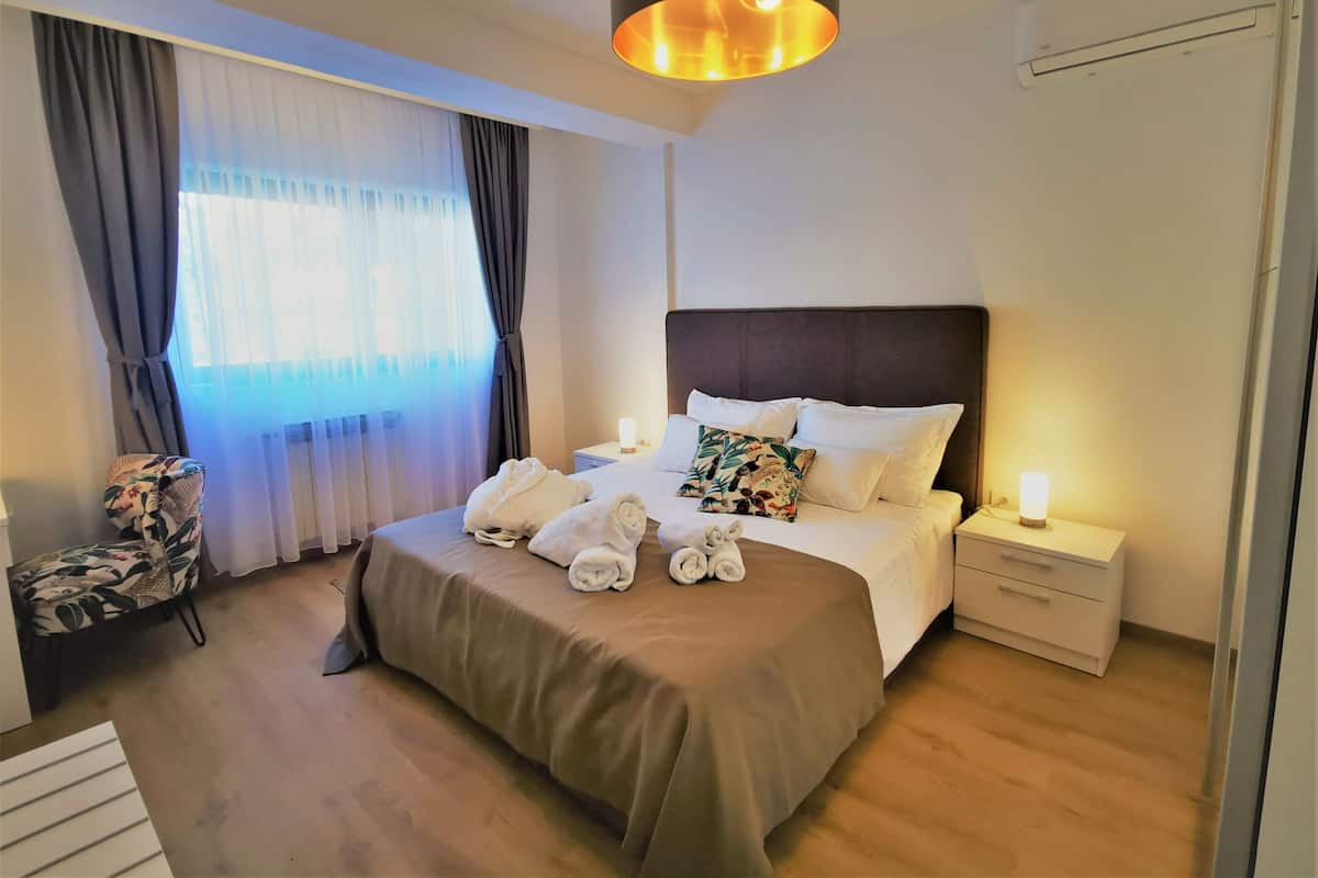 Une chambre d’hôtel avec un grand lit, une table de chevet avec une lampe, une chaise et une fenêtre avec des rideaux.