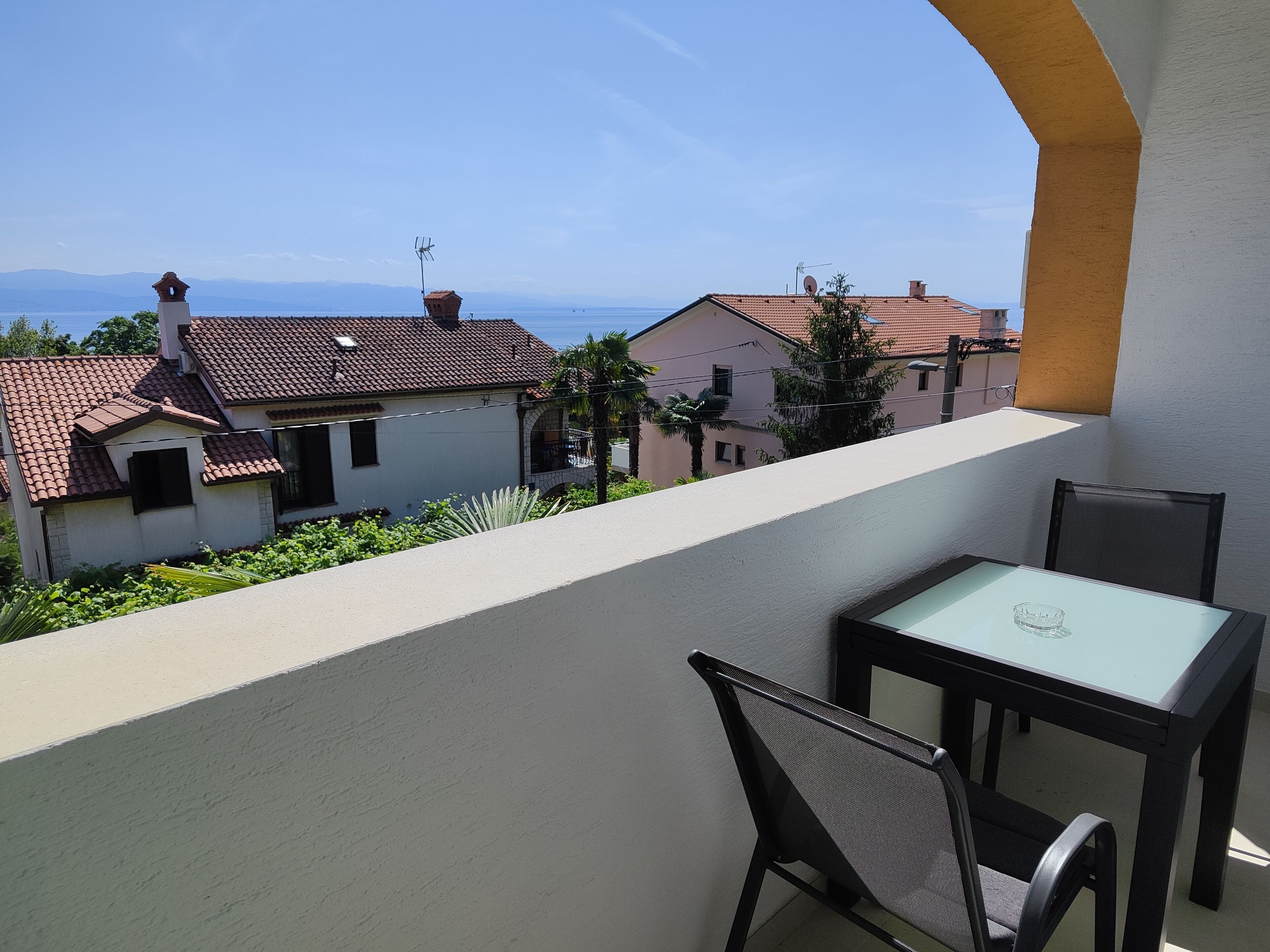 Un balcón con una mesa y sillas, con vista a una zona residencial con casas y una vista despejada del mar.