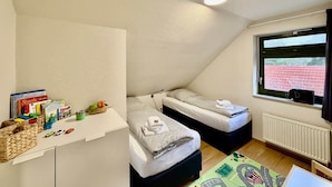 A small, triangular room with two beds, a white desk with books and toys, and a window with a view of a red fence. - Frisch Renoviertes, Sehr Modernes Ferienhaus für die Ganze Familie! (Varel)