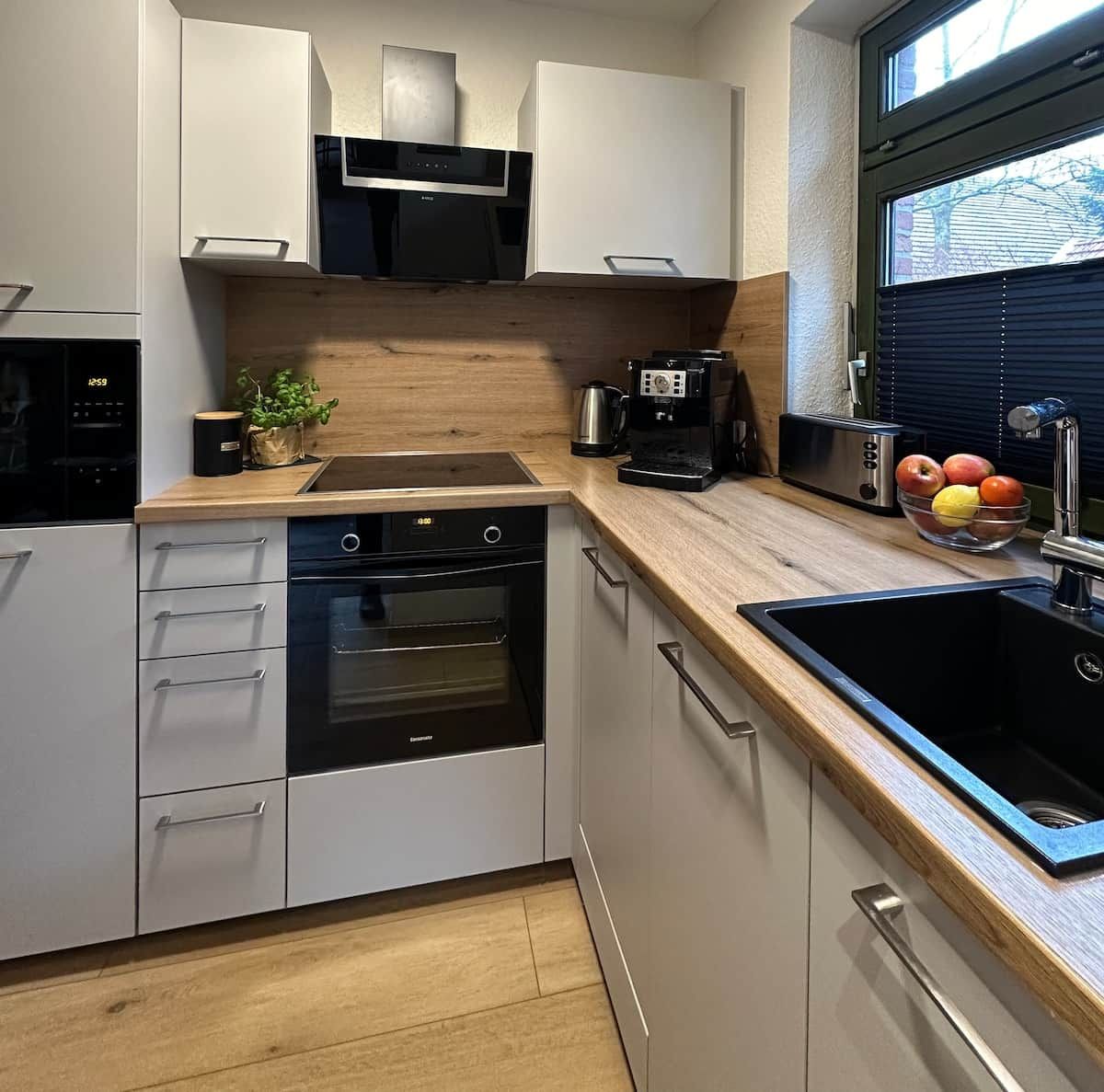 Una cocina moderna con electrodomésticos integrados, encimera de madera y ventana con persianas.