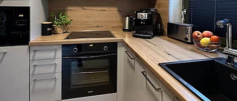 Una cocina moderna con electrodomésticos integrados, encimera de madera y ventana con persianas.