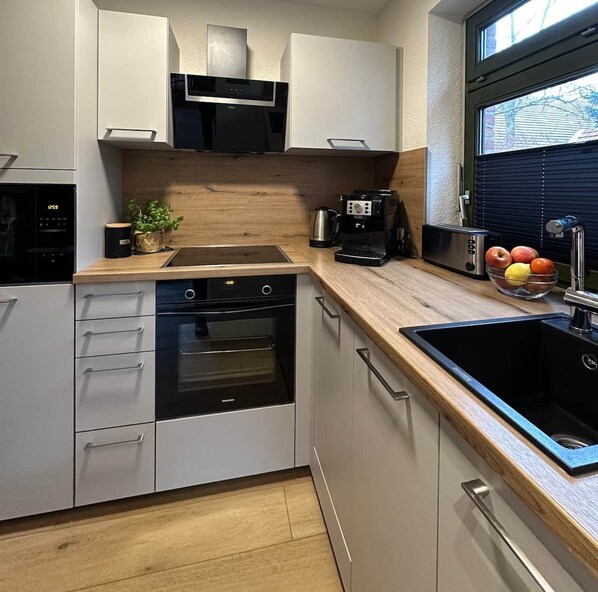 A modern kitchen with built-in appliances, a wooden countertop, and a window with blinds.