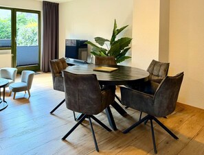 A modern dining area with a round table and six chairs, a potted plant, and a view of the outdoors through a window. - Frisch Renoviertes, Sehr Modernes Ferienhaus für die Ganze Familie! (Varel)