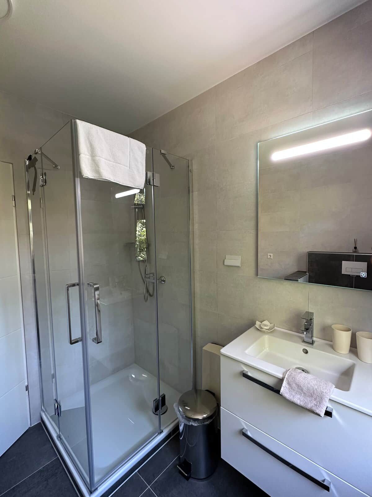 Un baño moderno con cabina de ducha de vidrio, un lavabo blanco y un espejo sobre el mueble.