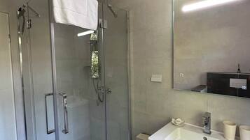 Un baño moderno con cabina de ducha de vidrio, un lavabo blanco y un espejo sobre el mueble.