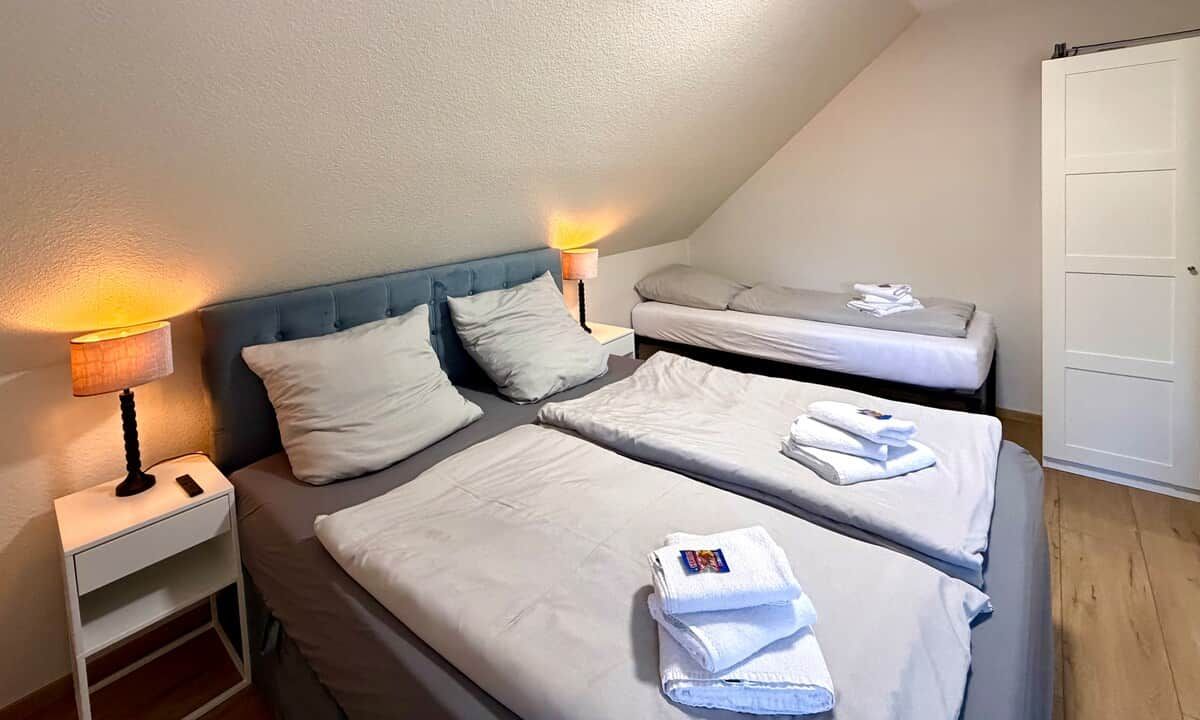 Una habitación con dos camas, una mesita de noche, una lámpara y una puerta.