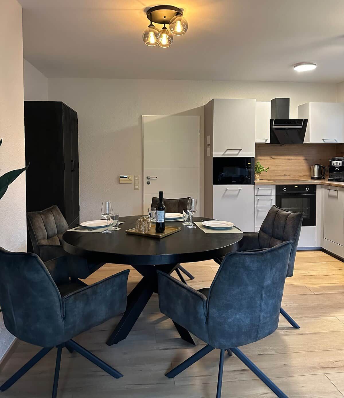 A modern dining area with a round table, four chairs, and a ceiling light fixture.