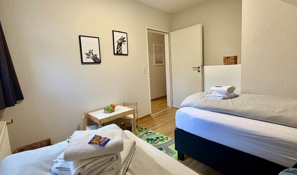 A hotel room with two beds, a small table, a chair, and a door leading to another room. - Frisch Renoviertes, Sehr Modernes Ferienhaus für die Ganze Familie! (Varel)