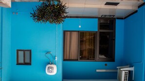 A room with a blue wall, a window with curtains, a small sink, and a radiator. - Praia De Tofo (Tofo)