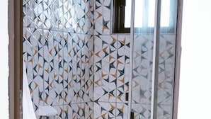 A bathroom with a geometric tile pattern, a white toilet, and a shower area. - Praia De Tofo (Tofo)