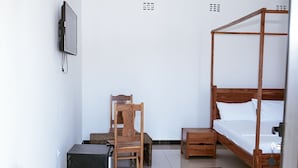 A bedroom with a four-poster bed, a wooden chair, a small table, and a TV mounted on the wall. - Praia De Tofo (Tofo)
