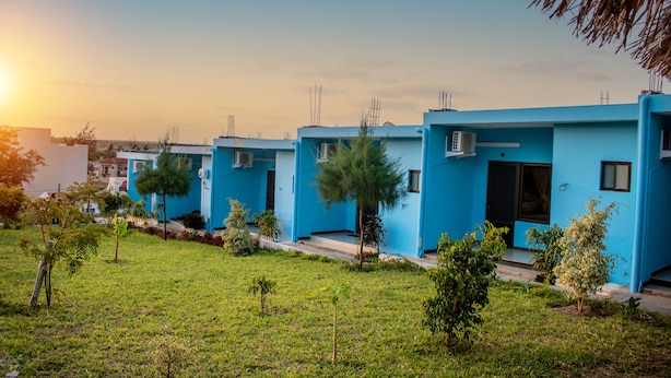 A row of blue buildings with air conditioning units, surrounded by small trees and grass. - Praia De Tofo (Tofo)