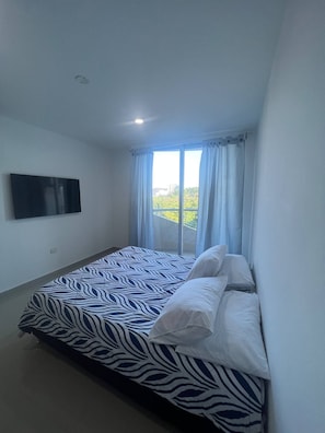 Un dormitorio con una cama, un televisor de pantalla plana y una ventana con cortinas.