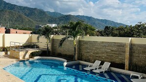 A swimming pool with clear blue water, surrounded by a tiled deck, and a view of mountains in the background. - Apartment In Bello Horizonte (Santa Marta)
