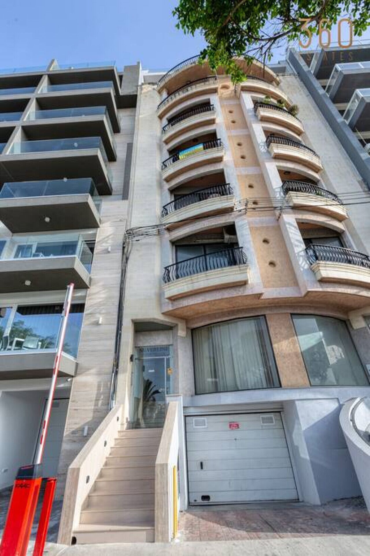 A multi-story residential building with balconies, a garage door, and a staircase leading to the entrance.