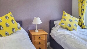 Une chambre avec deux lits, une table de chevet avec une lampe et des coussins jaunes ornés de motifs de hérissons.