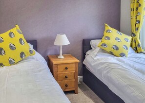 A bedroom with two beds, a nightstand with a lamp, and yellow pillows with hedgehog prints. - 2 bedroom accommodation in Thorney, Nr Lincoln (Thorney, Nr Lincoln)