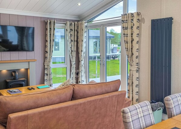 A living room with a sofa, a television, a fireplace, and large windows with curtains.