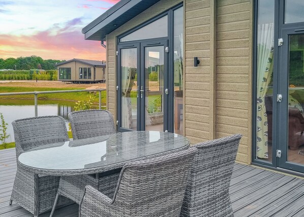 Une terrasse dotée de meubles en osier et de portes vitrées donnant sur une vue d’une maison et d’une étendue d’eau.