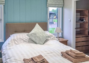 A neatly made bed with pillows, a bedside lamp, and towels, a window with a view of the outside, and a wooden wardrobe.