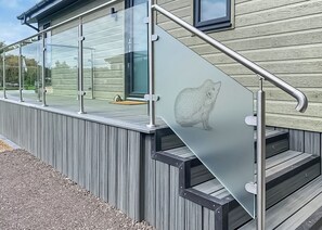 A modern building exterior with a glass balcony, metal railing, and a wooden deck.