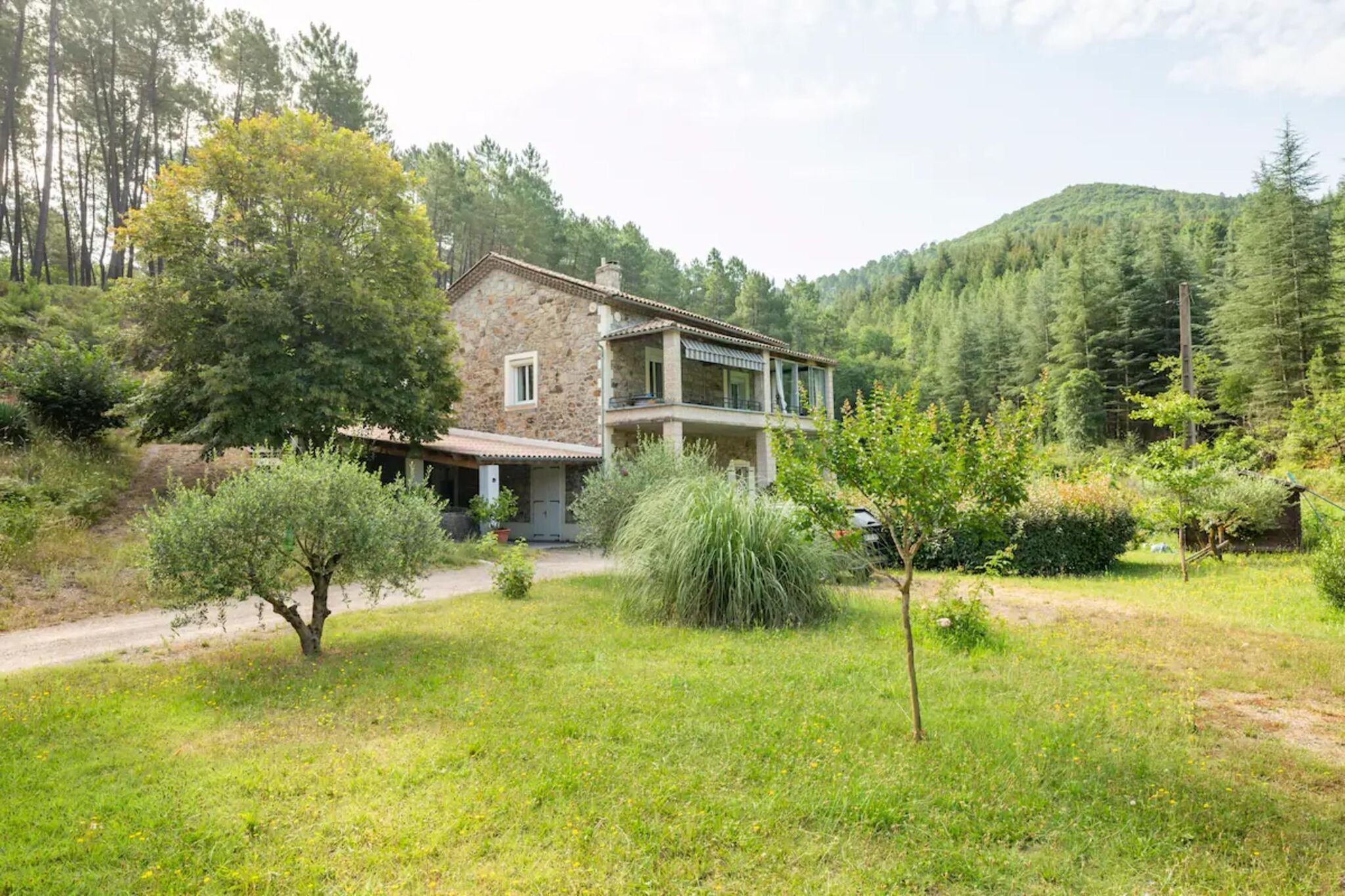 A stone house with a balcony, surrounded by a lush green landscape and trees.