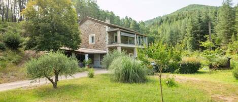 A stone house with a balcony, surrounded by a lush green landscape and trees.