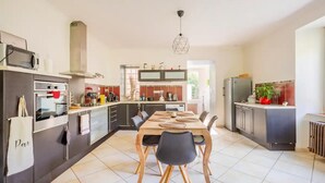 Una cocina moderna con comedor, que incluye una isla central, electrodomésticos integrados y una lámpara colgante.