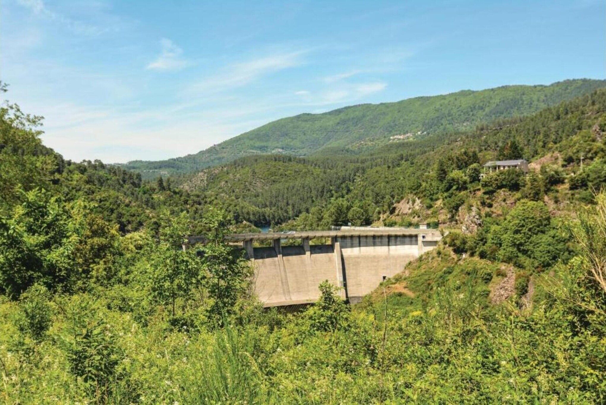 A dam with a concrete structure surrounded by lush greenery and hills.