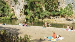 Una playa a orillas del río con gente tomando el sol y nadando, rodeada de riscos y vegetación.