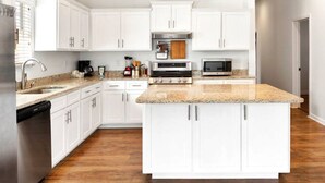 Una cocina moderna con armarios blancos, encimeras de granito, electrodomésticos de acero inoxidable y una isla central.