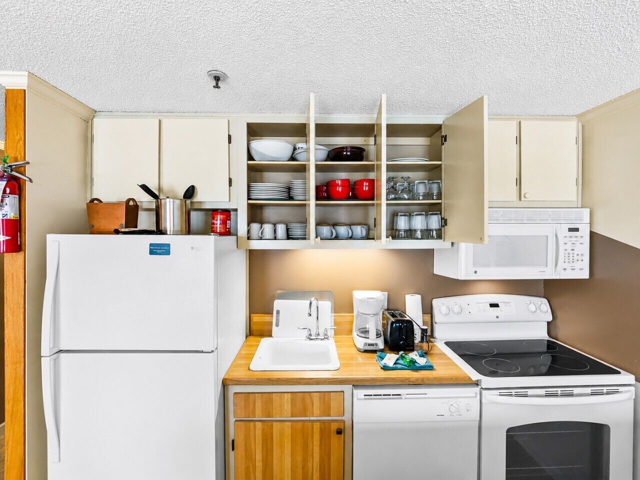A compact kitchenette with a refrigerator, microwave, stove, and a set of shelves above the counter.