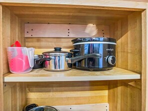 Una cocina con un estante de madera que sostiene una olla de cocción lenta, una olla y una taza medidora.