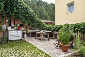 Un patio con una mesa y sillas, rodeado de plantas en macetas y una valla de madera.