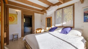 Un dormitorio con cama, vigas de madera, ventana y baño, además de un cuadro.
