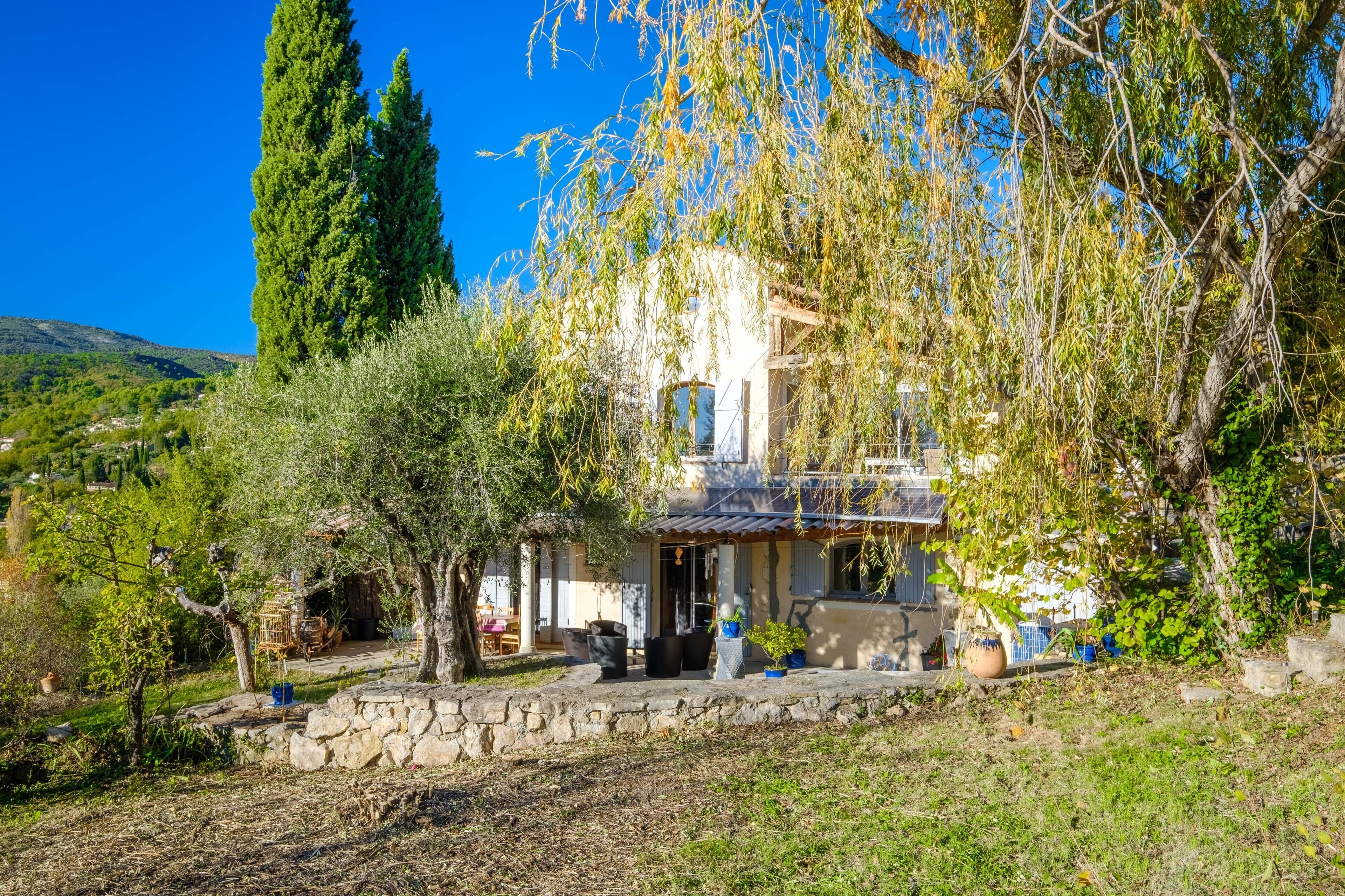 A house with a stone wall, a tree, and a view of the countryside.