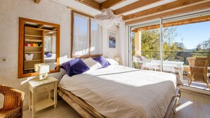 Un dormitorio con cama, mesita de noche, espejo, ventana y balcón con una silla.
