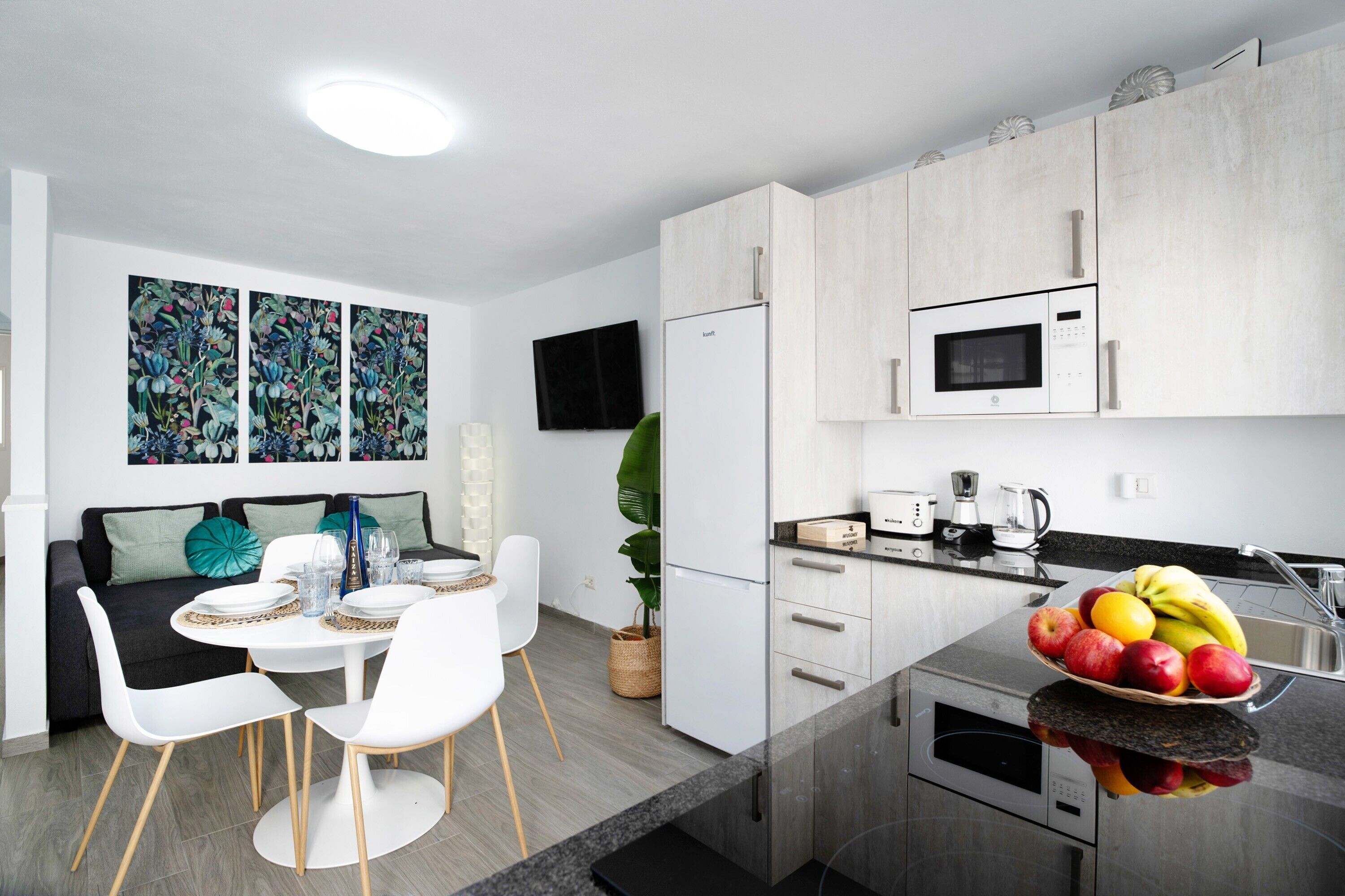 A modern kitchen with white cabinets, a microwave, and a fruit bowl on the counter.