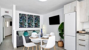 A modern kitchen with a white refrigerator, a dining table with white chairs, and a flat-screen TV mounted on the wall. - Holiday Home 'Casa Marion' with Private Terrace and Wi-Fi (El Golfo)