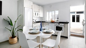 A modern kitchen with white cabinets, a dining table set with plates and glasses, and a potted plant. - Holiday Home 'Casa Marion' with Private Terrace and Wi-Fi (El Golfo)