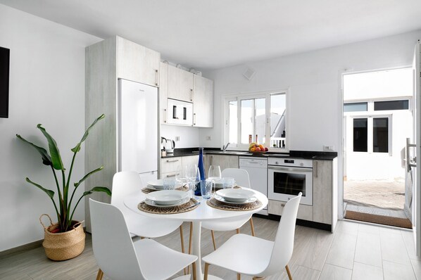 Una cocina moderna con armarios blancos, una mesa de comedor con platos y vasos, y una planta en maceta.