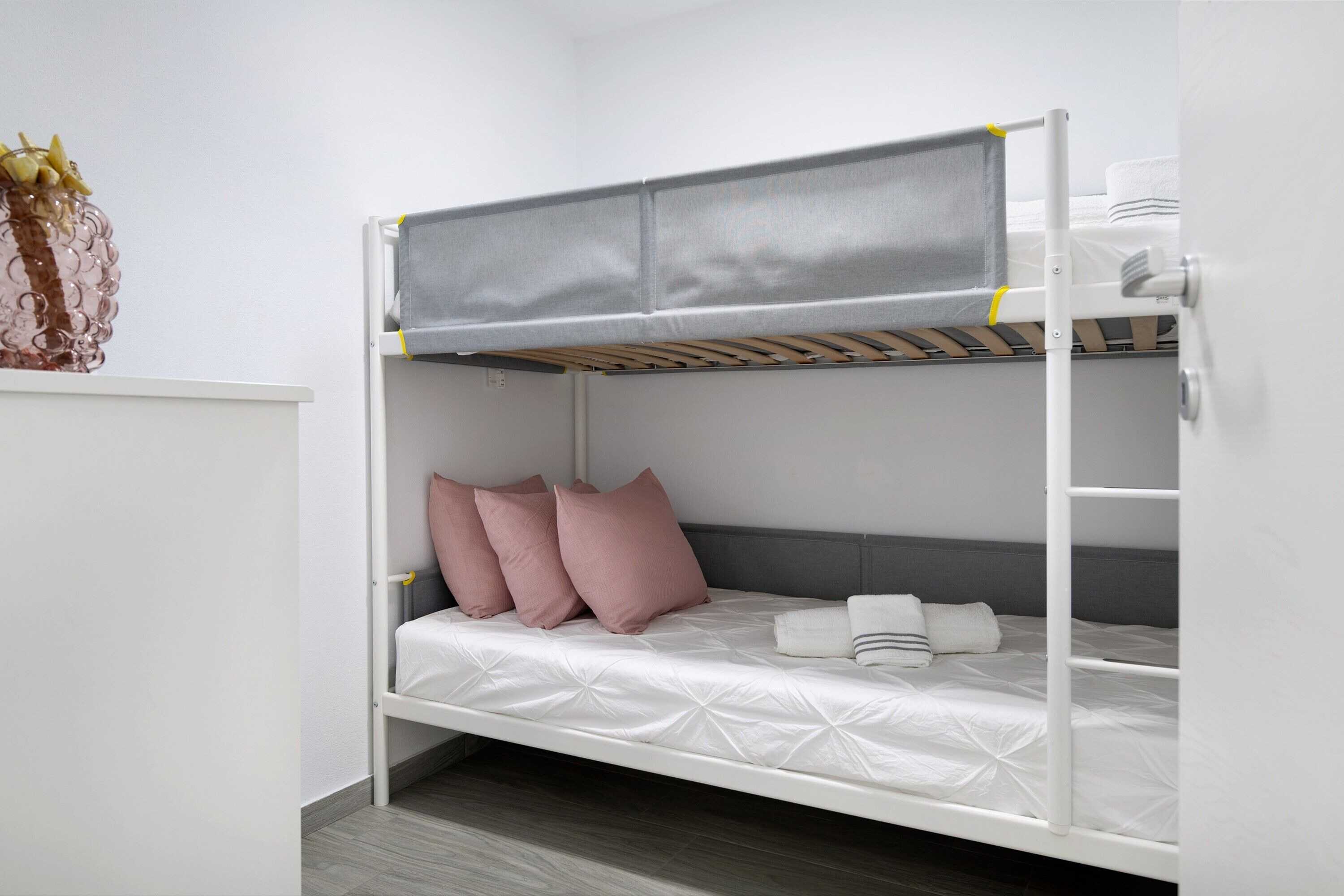 Una litera con un camarote superior gris y uno inferior blanco, almohadas y un estante con un adorno.