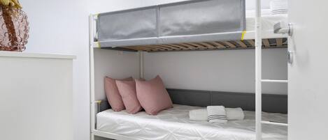 Una litera con un camarote superior gris y uno inferior blanco, almohadas y un estante con un adorno.