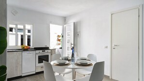 A modern kitchen with white appliances, a dining table set with plates and glasses, and a door leading to another room. - Holiday Home 'Casa Marion' with Private Terrace and Wi-Fi (El Golfo)