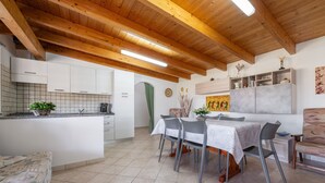 A kitchen with wooden beams, a dining area with chairs, and a tiled floor. - Vacation Home "Casa Silvia" with Private Terrace & Wi-Fi (Calasetta)