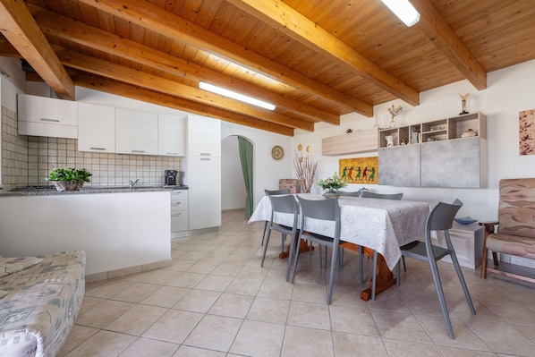 A kitchen with wooden beams, a dining area with chairs, and a tiled floor.
