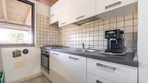 A kitchen with white cabinets, a gas stove, a coffee maker, and a window. - Vacation Home "Casa Silvia" with Private Terrace & Wi-Fi (Calasetta)