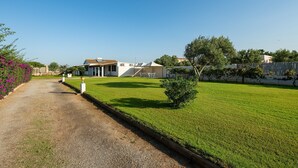 A residential property with a paved driveway, a well-maintained lawn, and a white building with a tiled roof. - Vacation Home "Casa Silvia" with Private Terrace & Wi-Fi (Calasetta)