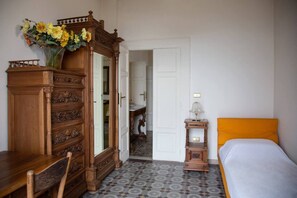 Un dormitorio con un aparador de madera, una cama con cabecera naranja, una mesita de noche y un jarrón con flores.